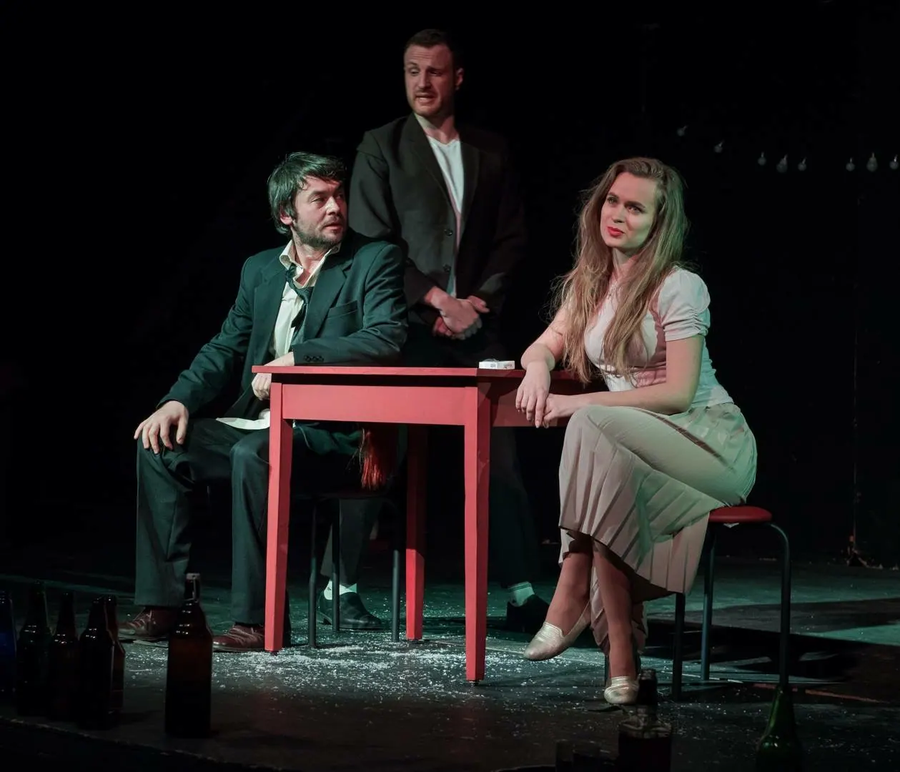 Krystyna with two scene partners at a red table on stage